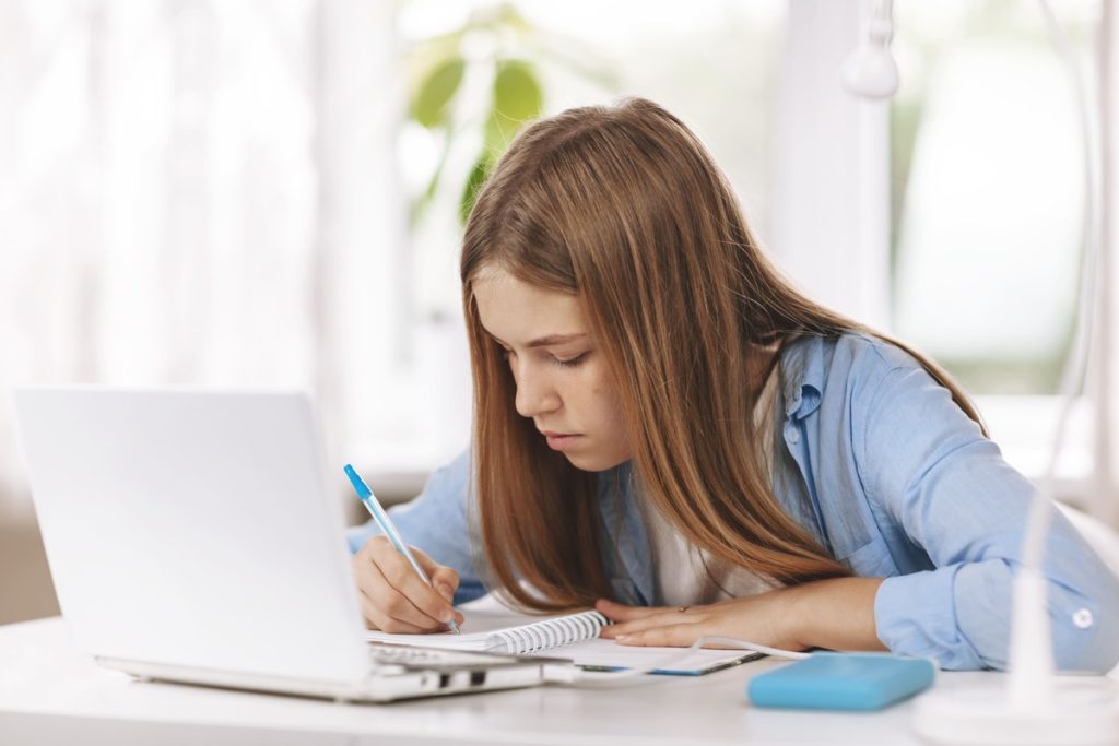 teenage-girl-taking-notes-while-studying-online-at-home